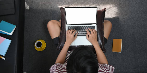 istock Top view image of creative man typing on white blank screen computer laptop that putting on his lap while sitting at the floor in comfortable living room. Work from home concept. 1222599216