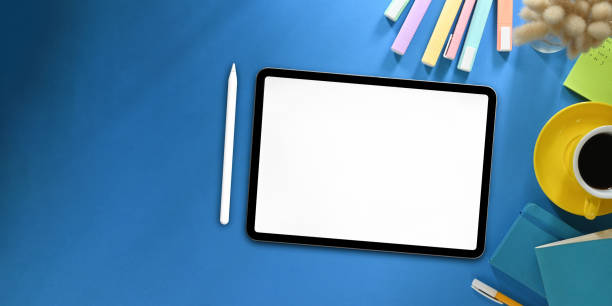 istock Top view image of white blanks screen computer tablet with stylus pen putting on colorful working desk and surrounded by marker pens, wild grass, coffee cup, note and pen. Orderly workspace concept. 1222599285