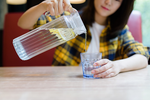 Young Asian woman pouring water into glass.