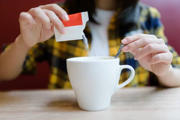 Young Asian woman pouring sugar into mug.