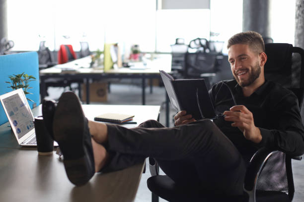 сосредоточенный современный бизнесмен работает и принимает к сведению в своем современном офисе, ноги на столе - 5956 стоковые фото и изображения