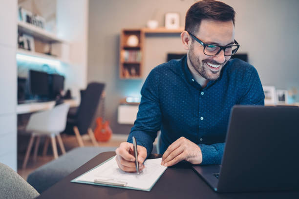 istock Smiling businessman looking at his laptop and writing in a document 1222605810
