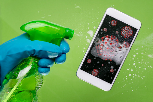 Woman with protective glove is spraying at mobile phone photographed from above on green background