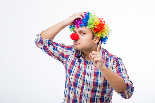 Comic male nerd in glasses and red clown nose making face and looking at camera on gray background