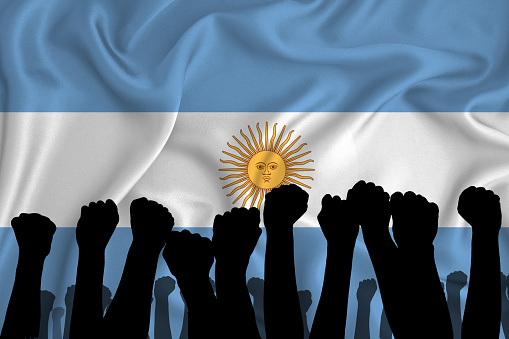Silhouette of raised arms and clenched fists on the background of the flag of Argentina. The concept of power, power, conflict. With place for your text.