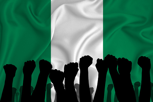 Silhouette of raised arms and clenched fists on the background of the flag of Nigeria. The concept of power, power, conflict. With place for your text.