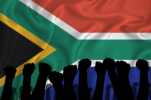 Silhouette of raised arms and clenched fists on the background of the flag of South Africa. The concept of power, power, conflict. With place for your text.