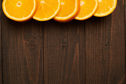 dark wooden background with blank space for text and fresh sliced orange fruits on side - natural and healthy food.