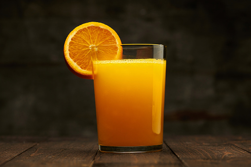 Fresh orange juice and fruit on a wooden table - natural and healthy food and drink. One glass of cocktail with a slice of fruit