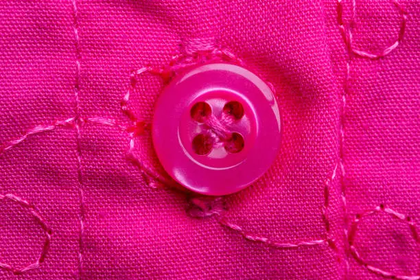 Macro photograph of a sewn-on pink button on a pink fabric with embroidery. Close-up detail of a little girls dress.