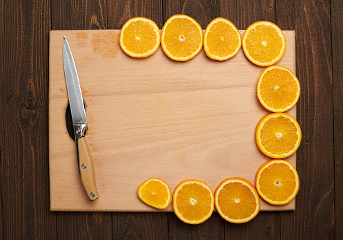 Fresh orange sliced fruits on a wooden table and cutting board with kitchen knife. Natural and healthy food. Arranged as a frame with blank space in center.