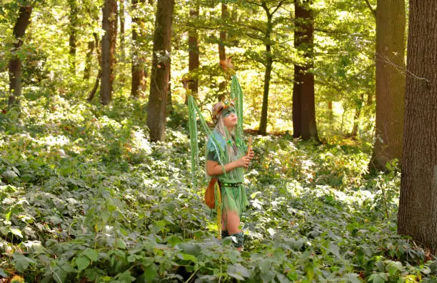 A young girl is dressed up as a fairy.
She is seen in a forest with her flute.