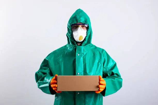 Man wearing impermeable suit with goggles and a mask standing against the white background with a box stock photo