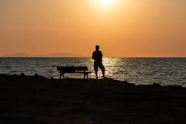 Silhouette of a fisherman on the shores of Altinkum Didim Turkey during sunset with orange skies over the shoreline.