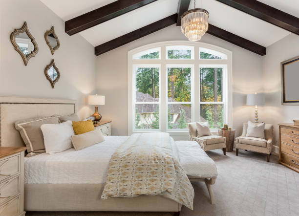 Master bedroom in new luxury home with chandelier and large bank of windows with view of trees stock photo
