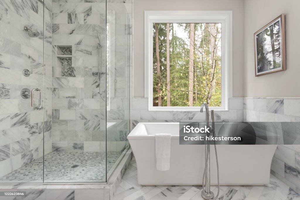 Master bathroom interior in luxury home with large shower with elegant tile and soaking bathtub. Includes large window with view of trees. Master bathroom shower and bathtub Bathroom Stock Photo