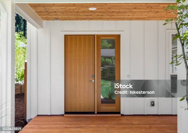 Covered Porch And Front Door Of Beautiful New Home Features White Siding And Rich Warm Wood Porch And Ceiling Door Is Closed Stock Photo - Download Image Now