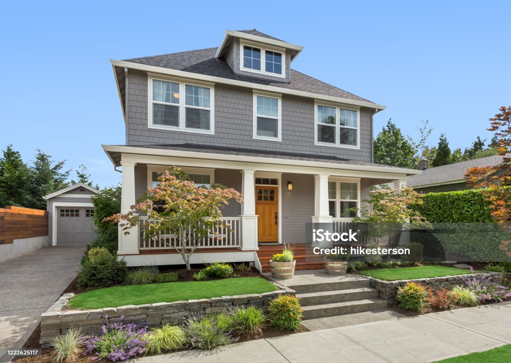 Beautiful craftsman home exterior on bright sunny day with green grass and blue sky facade of home with manicured lawn, and backdrop of trees and blue sky House Stock Photo