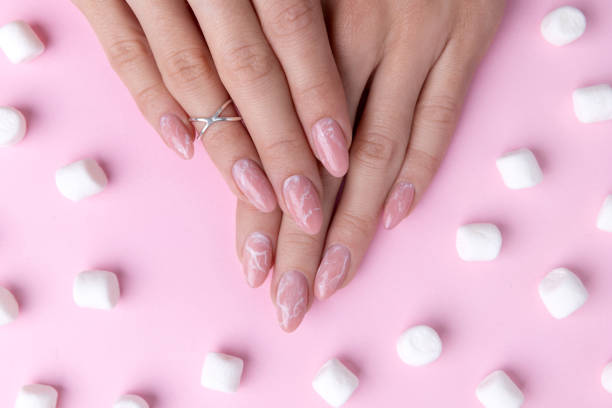 Womans hands with trendy marble manicure with marshmallows.