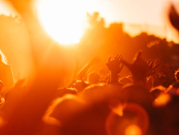 Crowd of people cheering at a music festival at sunset stock photo