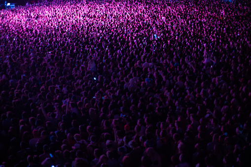 Crowd of people cheering at a music festival at night, a woman riding on her boyfriends shoulders
