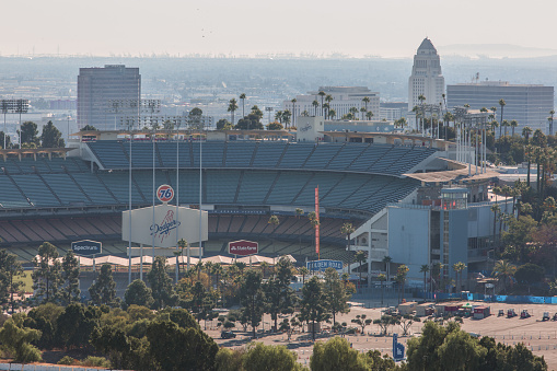Los Angeles, California, USA - November 11, 24 2019: Aerial view from helicopter of Los Angeles Dodger Stadium in Elysian Park, with the skyscraper skyline of Los Angeles in the smoggy background distance. The Stadium is just north of downtown Los Angeles and is the home of the Los Angeles Dodger major league baseball team. The stadium in this photo is empty at a time when no game is being played.