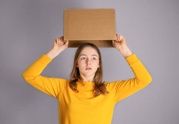 istock Teenager student girl taking cardboard box off her head having bright idea or plan. Think outside the box concept. Out of comfort zone. 1222631567