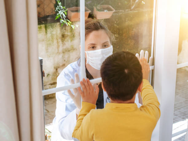 istock Healthcare worker posing seeing her son with a window glass separating them to avoid possible contagion 1222633471