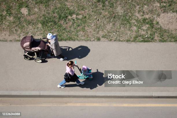 Mujeres Con Un Cochecito De Bebé Y Un Niño En Una Bicicleta De Juguete Caminando Por Una Calle De La Ciudad Foto de stock y más banco de imágenes de Top