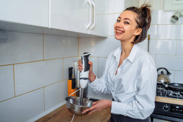 istock Attractive girl preparing dough in a food processor while standing in a bright kitchen. Mixing dough with hand mixer on kitchen table background with cooking ingredients 1222637921
