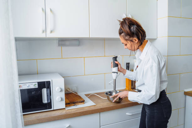 istock Attractive girl preparing dough in a food processor while standing in a bright kitchen. Mixing dough with hand mixer on kitchen table background with cooking ingredients 1222637927