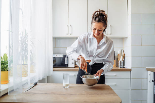 istock Attractive girl preparing dough in a food processor while standing in a bright kitchen. Mixing dough with hand mixer on kitchen table background with cooking ingredients 1222638054