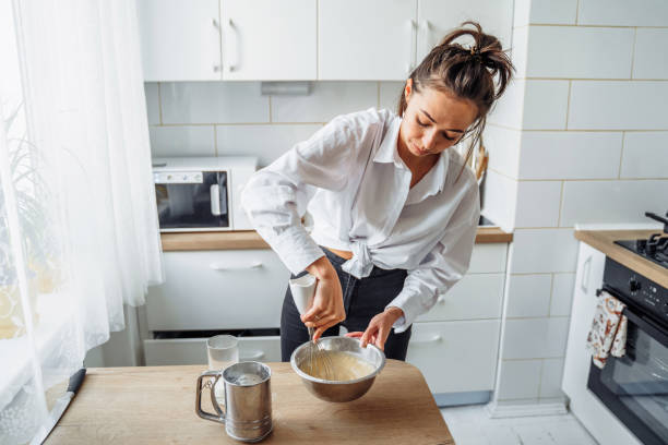istock Attractive girl preparing dough in a food processor while standing in a bright kitchen. Mixing dough with hand mixer on kitchen table background with cooking ingredients 1222638138