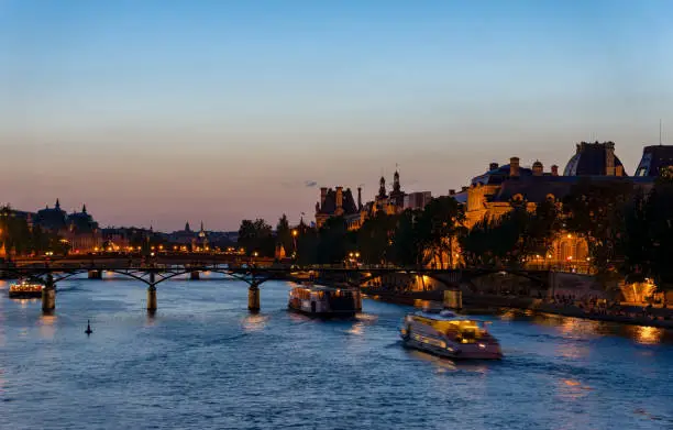Nightfall over Seine river and Pont des arts with palais royal and musee d'orsay in background - Paris, France
