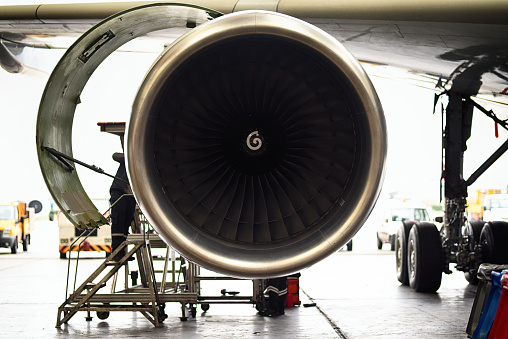 Aircraft engineer repairing and maintaining an airplane jet engine in airplane hangar