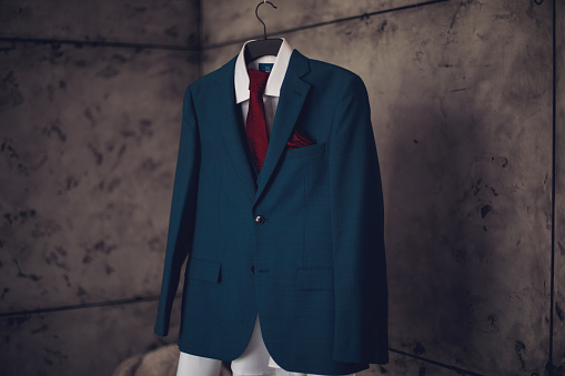 A blue suit with a red tie on a hanging hanger is waiting to be worn