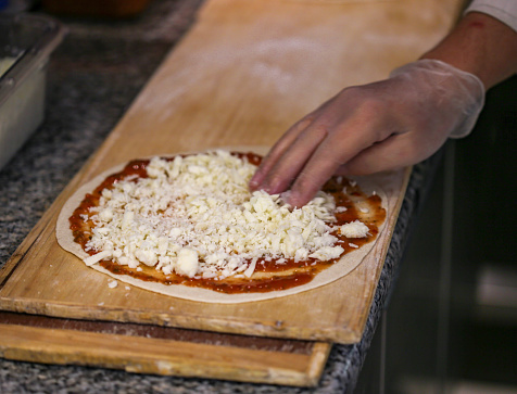 Pizza preparation. Adding cheese on lebanese pizza