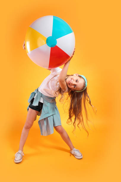 Funny happy child in summer clothes jumping with beachball on colored background Funny happy child in summer clothes jumping with beachball on colored yellow background beach ball beach summer ball stock pictures, royalty-free photos & images