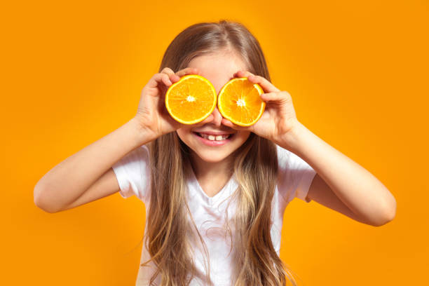 lustiges kleines mädchen mit zitrusfrüchten auf gelbem hintergrund - child bizarre little girls humor stock-fotos und bilder