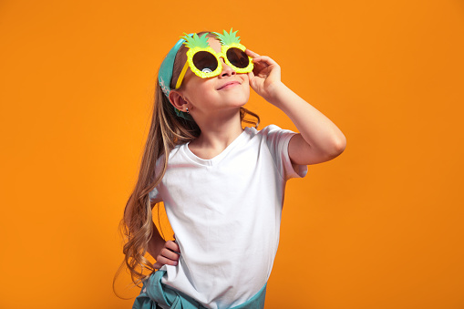 Smiling girl posing in the funny sunglasses and looking away on yellow studio background