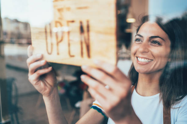 Small business Portrait of a happy business owner hanging an open sign on the door at a cafe and smiling cafeteria worker photos stock pictures, royalty-free photos & images