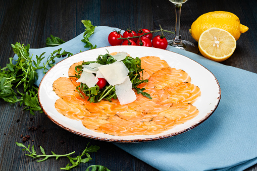 Salmon carpaccio served with arugula leaves, parmesan cheese and cherry tomatoes on white plate.