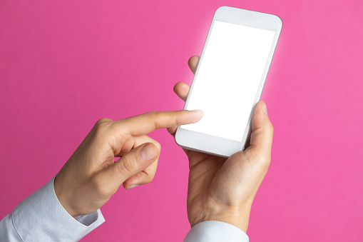 Unrecognizable person is showing screen of smart phone to camera and is pointing with one finger at device screen in front of pink background.