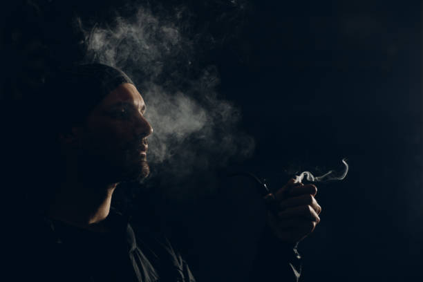 istock Man smoking a pipe on dark background. Profile portrait. 1222651193