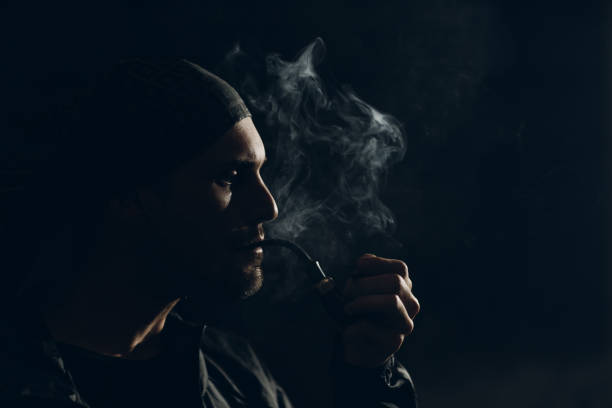 istock Man smoking a pipe on dark background. Profile portrait. 1222651202