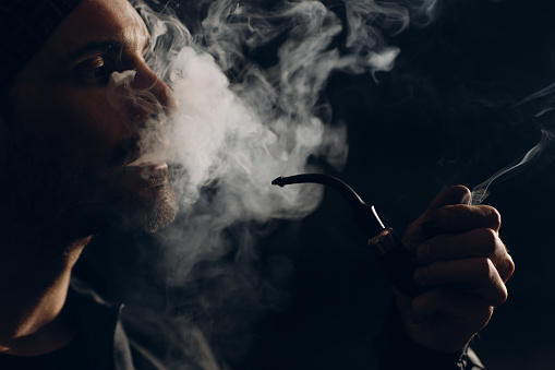 Man smoking a pipe on dark background. Back lit profile portrait.