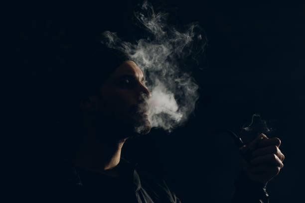 istock Man smoking a pipe on dark background. Profile portrait. 1222651213