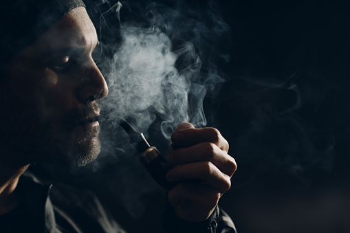 Man smoking a pipe on dark background. Back lit profile portrait.