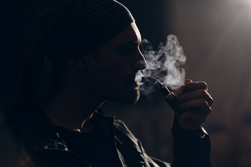 Man smoking a pipe on dark background. Profile portrait back lit.