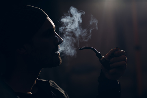 Man smoking a pipe on dark background. Profile portrait back lit.